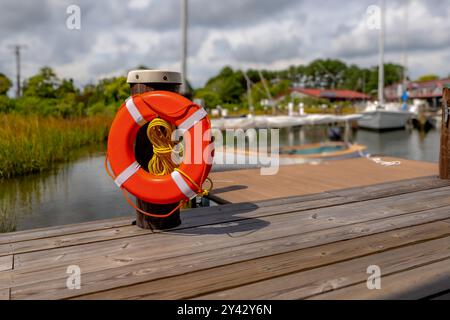 Orangefarbener Rettungsring, Hafenlebensretter, montiert auf einem Dockenstapel mit einem gelben Nylonseil. Stockfoto