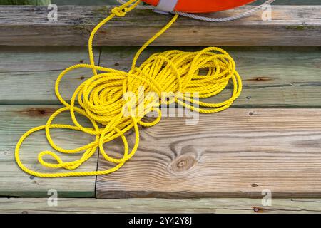 Gelbes Nylonseil, verbunden mit einem orangefarbenen Rettungsring, sitzend auf einem hölzernen Dock, Pier. Stockfoto