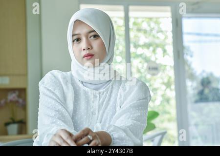 Pose einer jungen Frau, die einen weißen Hijab in einem Café trägt. Begleitet von einem Glas Eiskaffee Stockfoto