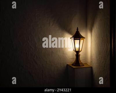 Alte schwarze Vintage Pfostenlampe strahlt ein warmes gelbes Licht aus, Dekoration, stehend allein auf einem weißen Wandhintergrund mit Kopierraum. Straßenlaterne bei t Stockfoto