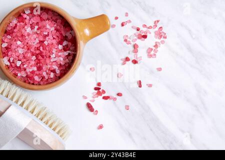 Rosafarbenes Himalaya-Salz in einer Keramikschale mit einer Holzbürste auf einer weißen Marmoroberfläche. Dieses Bild eignet sich perfekt für Beauty-, Spa- und Wellnesskonzepte Stockfoto