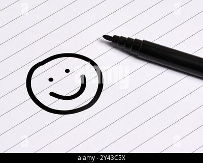 Handgezeichnetes lächelndes Gesicht auf einem Notizbuch mit Stift. Positivitäts-, Glücks- und Zufriedenheitskonzept. Stockfoto