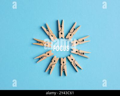 Fokussierung und Konzentration auf das Geschäfts- oder Bildungskonzept. Hölzerne Miniatur-Kleiderschalen bilden einen kreisförmigen Rahmen mit dem Wort Fokus auf blauem Hintergrund Stockfoto