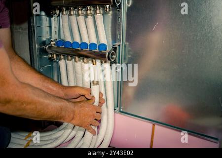 Arbeiter montieren neue Verteilerventile aus Messing für Zentralheizungsböden in einem im Bau befindlichen Wohngebäude. Stockfoto