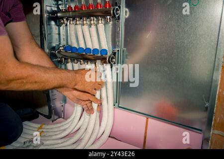 Arbeiter montieren neue Verteilerventile aus Messing für Zentralheizungsböden in einem im Bau befindlichen Wohngebäude. Stockfoto