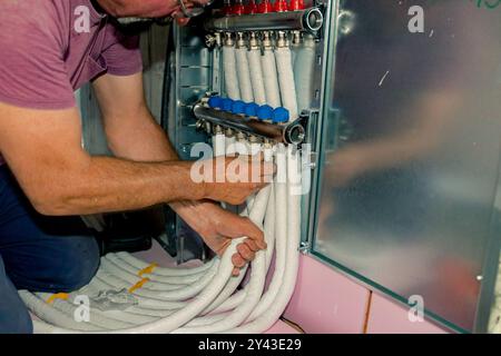 Arbeiter montieren neue Verteilerventile aus Messing für Zentralheizungsböden in einem im Bau befindlichen Wohngebäude. Stockfoto