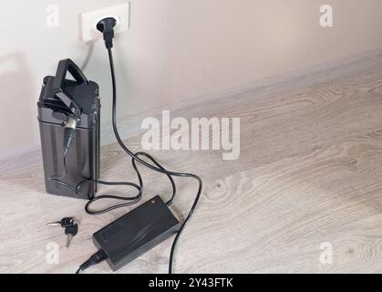 Laden der Fahrradbatterie über das Stromnetz im Haus. Steckdose im Zimmer mit eingeschaltetem Stecker. Umweltfreundlicher Transport. Stockfoto