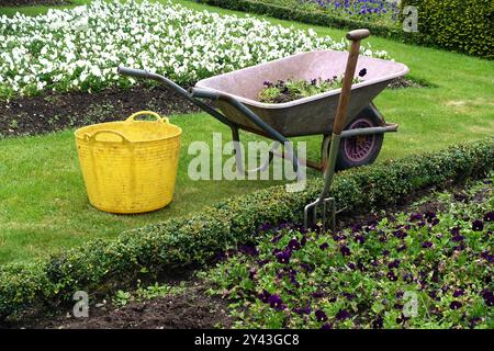 Yellow Gardening Eimer & Wheelbarrow in Levens Hall Manor House Gardens im Lake District National Park, Cumbria, England, Großbritannien. Stockfoto