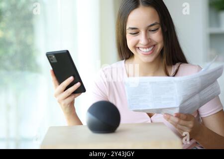 Glückliche Frau, die intelligente Lautsprecheranleitungen liest, die das Telefon zu Hause hält Stockfoto