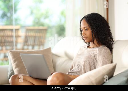 Ernste schwarze Frau, die zu Hause auf einer Couch sitzt Stockfoto