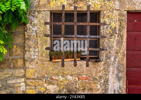 Altes Fenster mit Eisengitter und Besen auf der Fensterbank in einer kleinen Stadt in Kroatien Stockfoto