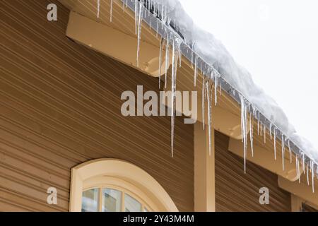 Eiszapfen hängen am Dachrand eines hölzernen Wohnhauses Stockfoto