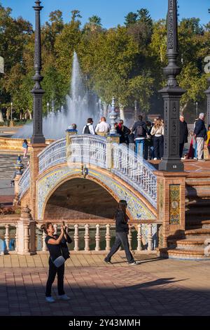 Sevilla, Spanien - 24. Oktober 2023: Menschen an der Plaza de Espana mit Brücke über Kanal und Brunnen im Maria Luisa Park, Wahrzeichen der Stadt. Stockfoto