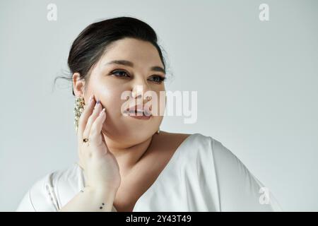 Eine atemberaubende Braut in Übergröße zeigt ihre Schönheit mit einem Brautkleid und Ohrringen, die Selbstvertrauen und Anmut ausstrahlt. Stockfoto