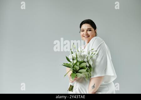 Eine strahlende Braut in Übergröße hält einen üppigen Blumenstrauß, trägt elegante Ohrringe und ein fließendes weißes Kleid. Stockfoto