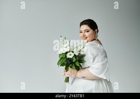 Eine strahlende Braut umarmt ihre Schönheit, trägt ein fließendes weißes Kleid und hält einen üppigen Blumenstrauß. Stockfoto