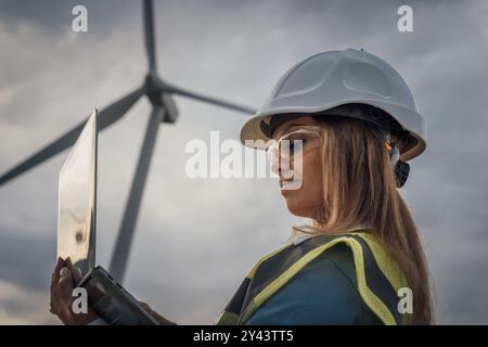 Eine talentierte Ingenieurin überwacht Windturbinen aktiv mit ihrem Laptop im dynamischen und innovativen Bereich erneuerbarer Energien und konzentriert sich dabei auf die Themen Stockfoto