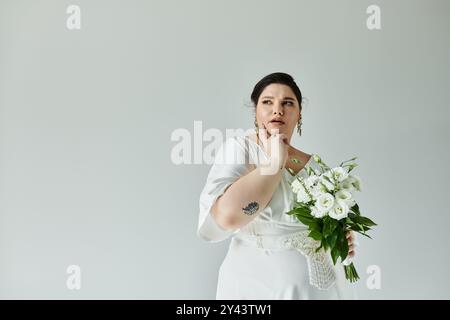 Eine atemberaubende Braut posiert anmutig, in einem weißen Kleid verziert und mit einem Blumenstrauß, strahlend Eleganz. Stockfoto