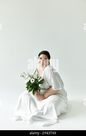 Die fröhliche Braut in einem fließenden Kleid umschmeichelt ihre Schönheit und hält einen frischen Blumenstrauß, der Glück versprüht. Stockfoto