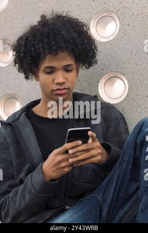 Teenager mit lockigem Haar, das Handy benutzt Stockfoto