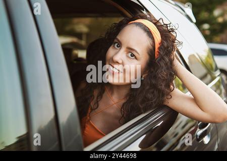 Eine junge Frau lächelt an einem sonnigen Tag aus dem Autofenster Stockfoto