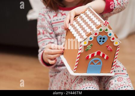 Nahaufnahme eines selbstgemachten Mädchens, das Lebkuchenhaus handgemacht macht. Weihnachtstradition Stockfoto
