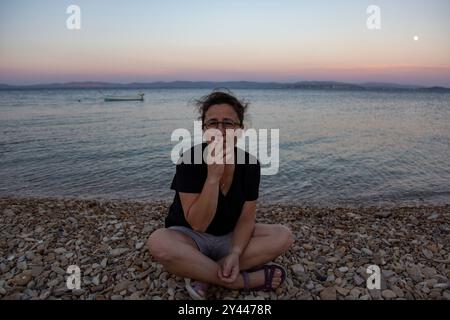 Reife Frau mit Brille raucht am Strand bei Sonnenuntergang Stockfoto