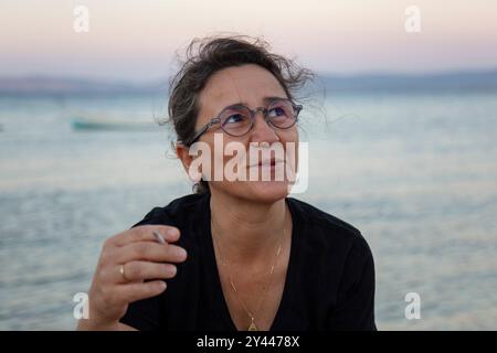 Reife Frau mit Brille raucht am Strand bei Sonnenuntergang Stockfoto