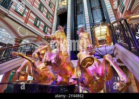 Asiatisches Kreuzfahrtschiff farbenfrohes Atrium, Treppen, Lobby, Innenraum, goldene Pferde, die eine Statue aufziehen, Panoramablick-Glasaufzüge, Star Cruises Superstar Virgo Stockfoto