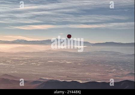 Ein roter Heißluftballon, der an einem klaren Frühlingstag über die Wüste in der Nähe von Marrakesch, Marokko, mit dem schneebedeckten Atlasgebirge im Hintergrund schwimmt Stockfoto