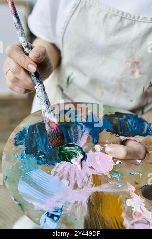 Eine Künstlerin mischt Farben auf ihrer Palette, die in ihrem Atelier in die Schöpfung eingetaucht ist. Stockfoto