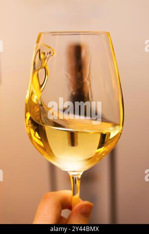 Ein wunderschöner Wein spritzt in einem Glas Weißwein, gehalten von einer Hand, die den Wein vor einem verschwommenen Hintergrund schwenkt Stockfoto