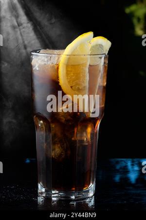 Cocktail in einem Highball mit Cola- und Zitronenscheiben vor dunklem Hintergrund Stockfoto