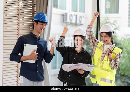 Gruppe von Happy Engineers feiert den Erfolg auf der Baustelle mit Blaupausen und Sicherheitsausrüstung Stockfoto