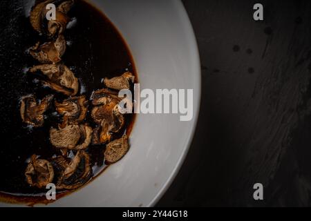 Getrocknete Pilze werden in Thai-Sauce in einer weißen Schüssel auf schwarzem Hintergrund mariniert. Hochwertige Fotos Stockfoto