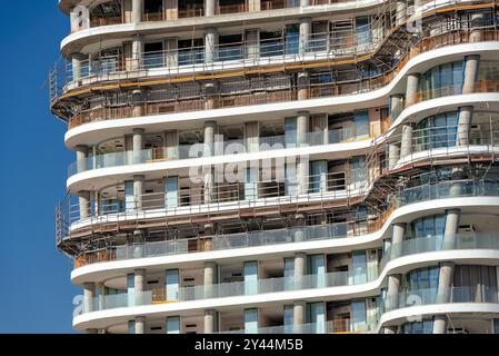 Die geschwungenen Balkone eines modernen Apartmenthauses sind noch immer mit Gerüsten in Ayia Napa Marina, Zypern, bedeckt Stockfoto