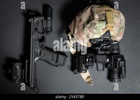 Taktische Ausrüstung und Waffen, Kappe und binokulares Nachtsichtgerät, Pistole mit Hinterschaft, Rotpunktvisier und Taschenlampe. Stockfoto