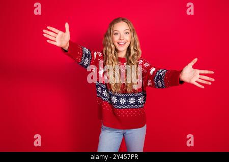 Foto der attraktiven Teenager Frau Stretch Hände Willkommen gekleidete stilvolle Ornament weihnachtskleidung Mottoparty auf rotem Hintergrund Stockfoto