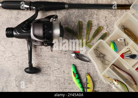 Angelköder, Haken und Angelrute mit Spinnrolle auf grauem Tisch, Ansicht oben Stockfoto