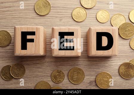 Würfel mit den Buchstaben Fed (Federal Reserve System) und Münzen auf Holztisch, flach gelegt Stockfoto