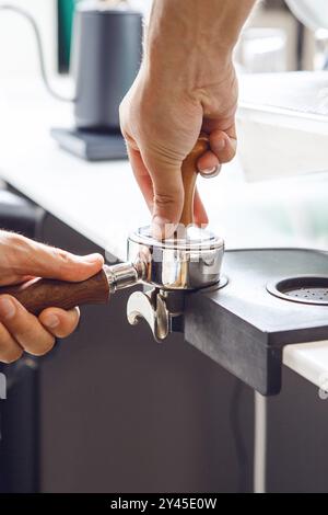 Nahaufnahme von Barista, der Espresso im Portafilter auf der Arbeitsfläche während der Kaffeezubereitung stampft Stockfoto