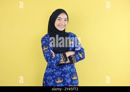 Eine junge indonesische Frau in Hijab und Korpri Batik Blue Uniform zeigt selbstbewusste Geste, indem sie ihre Arme faltet. Indonesischer Mitarbeiter der ASN-Regierung Stockfoto