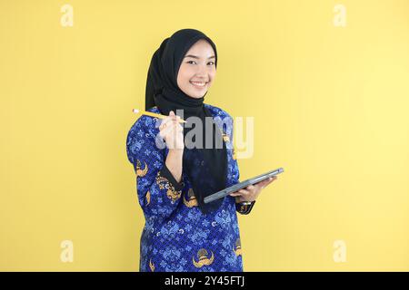 Fröhliche muslimische Regierungsangestellte oder ASN-Frau in blauer Korpri Batik Uniform, die Lasche und Stift auslöscht Stockfoto