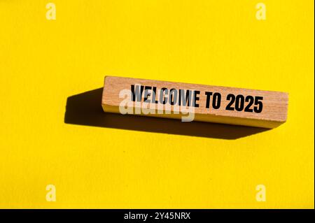 Willkommen bei 2025 Nachricht auf Holzblock mit gelbem Hintergrund. Konzeptionelles Willkommen bei 2025 Symbol. Kopierbereich. Stockfoto