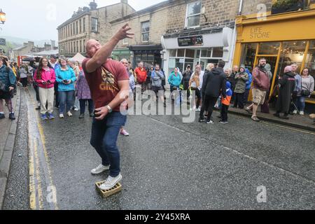 8. September 2024. Ramsbottom, Bury, Lancashire UK. Die Weltmeisterschaft Im Schwarzen Pudding-Werfen. Die Teilnehmer stehen auf einem „goldenen Gitter“, das feierlich auf die Bridge Street im Dorf Ramsbottom geführt und an der Tür des Oaks Public House platziert wird. Die Teilnehmer stehen mit einem Fuß auf der Startaufstellung, und mit einem „Lob“ unter den Armen schleudern 3 schwarze Puddings von Chadwicks of Bury auf 12 Yorkshire Puddings auf einem Sockel 30 Fuß/6 Meter hoch auf einem Gerüst. Der Sport steht für die Rivalität zwischen den benachbarten englischen Countys Lancashire und Yorkshire, die auf den Krieg zurückgeht Stockfoto