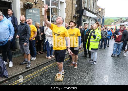 8. September 2024. Ramsbottom, Bury, Lancashire UK. Die Weltmeisterschaft Im Schwarzen Pudding-Werfen. Die Teilnehmer stehen auf einem „goldenen Gitter“, das feierlich auf die Bridge Street im Dorf Ramsbottom geführt und an der Tür des Oaks Public House platziert wird. Die Teilnehmer stehen mit einem Fuß auf der Startaufstellung, und mit einem „Lob“ unter den Armen schleudern 3 schwarze Puddings von Chadwicks of Bury auf 12 Yorkshire Puddings auf einem Sockel 30 Fuß/6 Meter hoch auf einem Gerüst. Der Sport steht für die Rivalität zwischen den benachbarten englischen Countys Lancashire und Yorkshire, die auf den Krieg zurückgeht Stockfoto