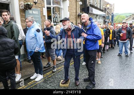 8. September 2024. Ramsbottom, Bury, Lancashire UK. Die Weltmeisterschaft Im Schwarzen Pudding-Werfen. Die Teilnehmer stehen auf einem „goldenen Gitter“, das feierlich auf die Bridge Street im Dorf Ramsbottom geführt und an der Tür des Oaks Public House platziert wird. Die Teilnehmer stehen mit einem Fuß auf der Startaufstellung, und mit einem „Lob“ unter den Armen schleudern 3 schwarze Puddings von Chadwicks of Bury auf 12 Yorkshire Puddings auf einem Sockel 30 Fuß/6 Meter hoch auf einem Gerüst. Der Sport steht für die Rivalität zwischen den benachbarten englischen Countys Lancashire und Yorkshire, die auf den Krieg zurückgeht Stockfoto