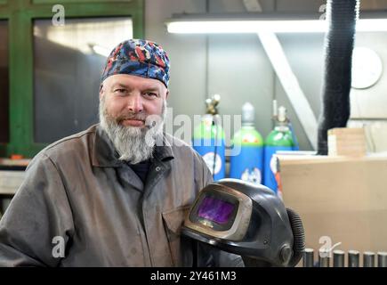 Porträt eines älteren Arbeiters in der Gießerei in Arbeitskleidung - Schweißer mit Schutzhelm, der in die Kamera blickt - Nahaufnahme Stockfoto