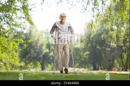 Älterer Mann mit verletzten Beinen, der mit Krücken im Park steht Stockfoto