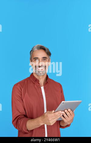 Glücklicher reifer Mann, der ein digitales Tablet benutzt, das isoliert auf blauem Hintergrund steht. Stockfoto